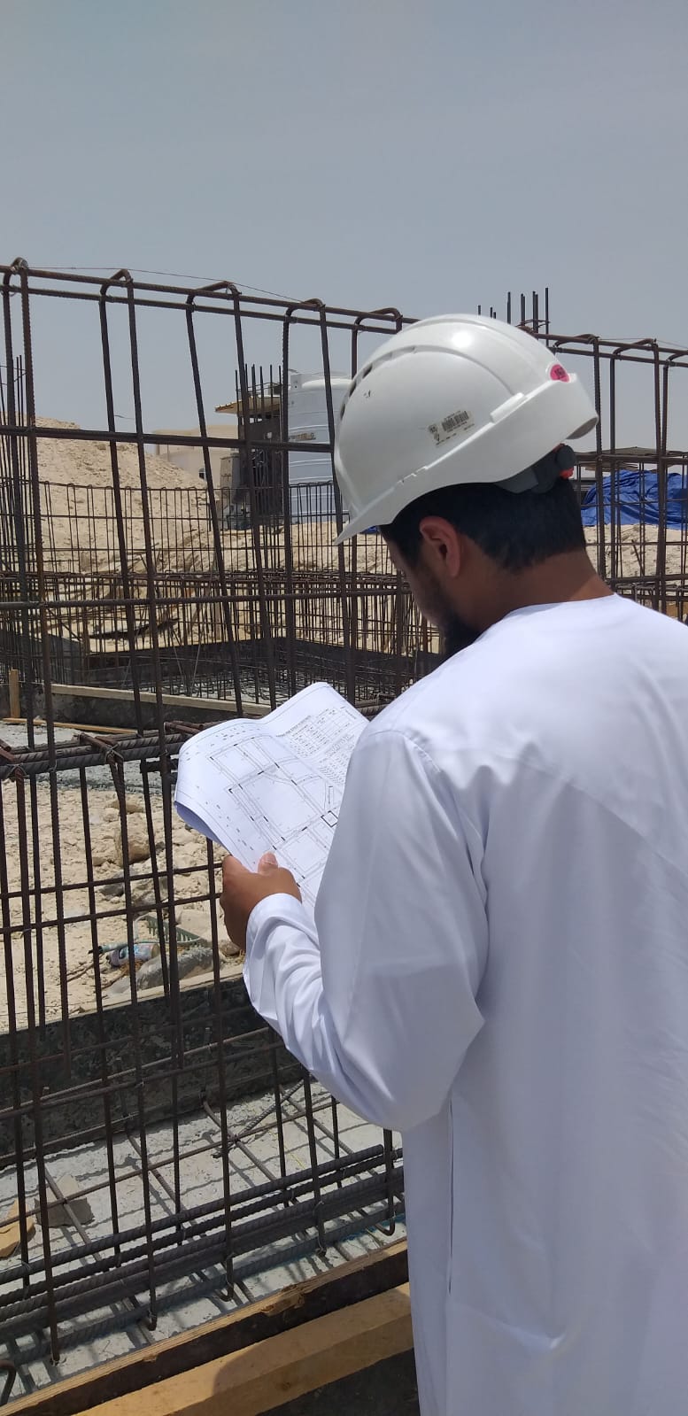 Municipality engineer reviewing approved drawings beside the rebar cages in Baniyas.