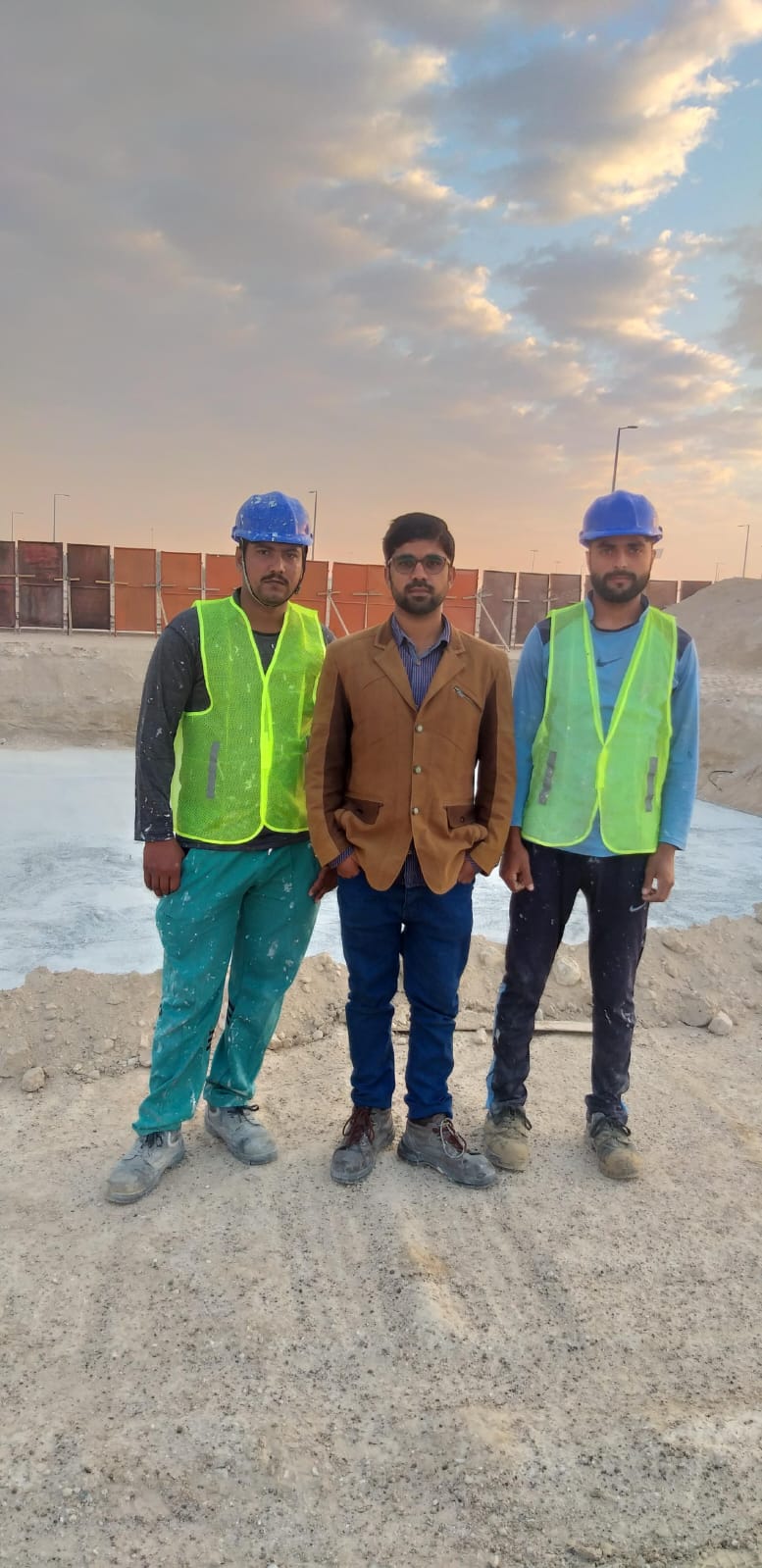 Engr. Muhammad Tayyab standing with two Build Marque crew members on the Baniyas site at sunset.