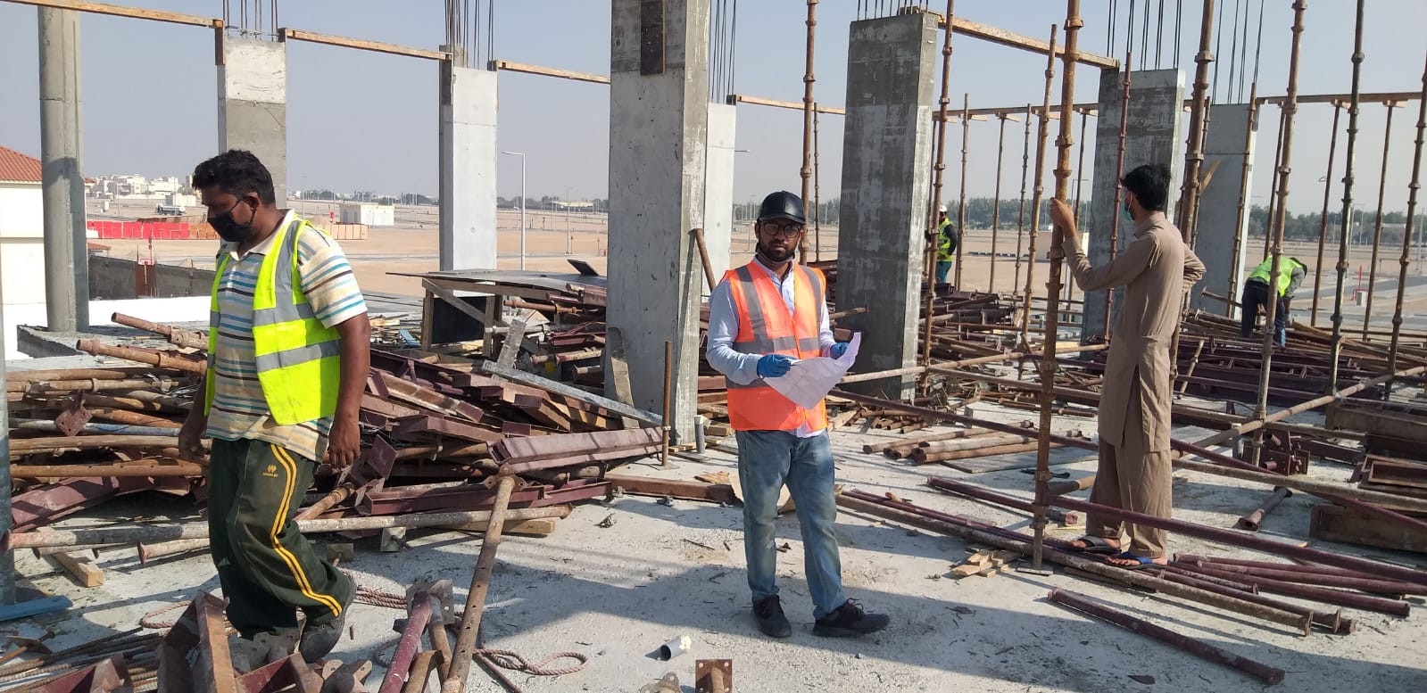 Engr. Tayyab in hi-vis reading structural drawings on the slab deck in Baniyas.