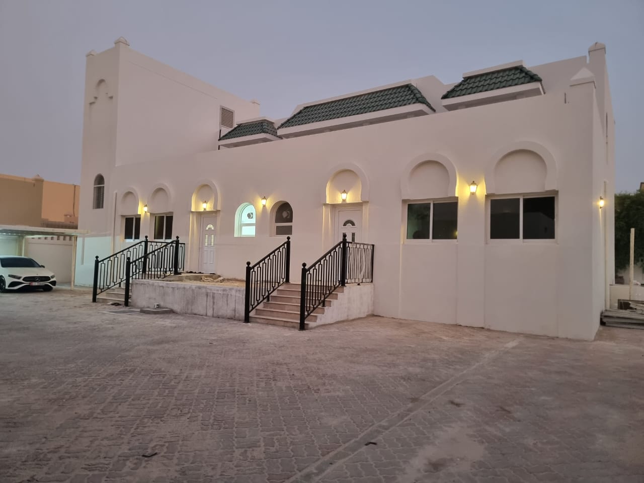 Completed Al Helia villa exterior at dusk, with black wrought-iron railings and arched facade.
